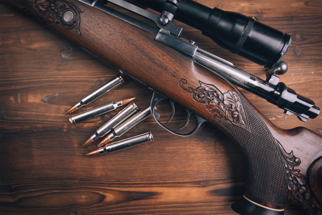 Gevär med träkolv, graverad låda, kikarsikte och ammunition på ett träbord